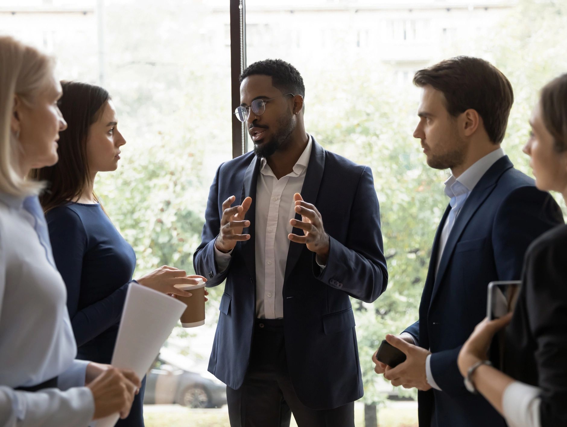A group of professionals stands talking as one person speaks and gestures during a discussion.
