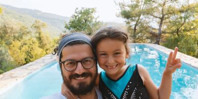 A man and girl smiling by a pool, taking a selfie outdoors.