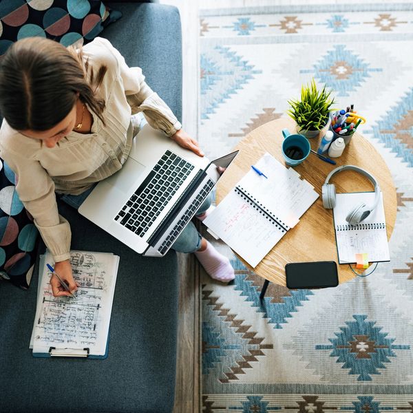 Photo of a woman on a computer writing on a notepad with a small round table in front of her