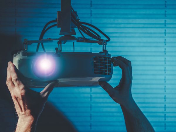 Hands adjusting a ceiling-mounted projector emitting light.