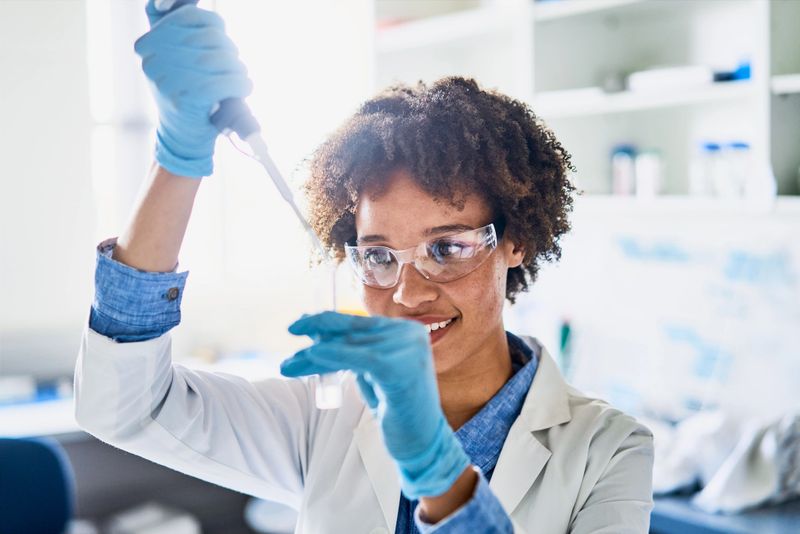 Smiling young female scientist using a pipette while working with research samples