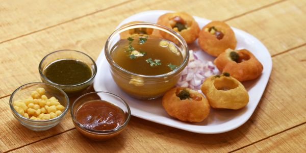 Plate of pani puri with accompaniments on a wooden table.