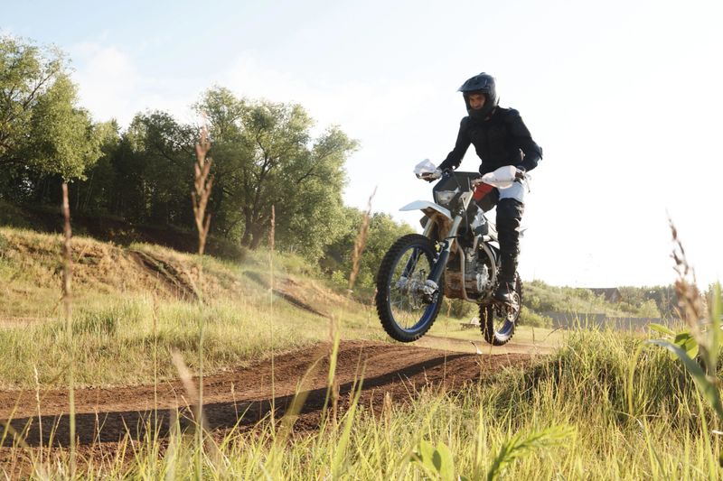 Extreme man in protective wear being in mid air while riding motorbike on hills at competition