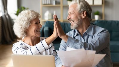 Elderly couple holds papers in hands while high-fiving and smiling.
