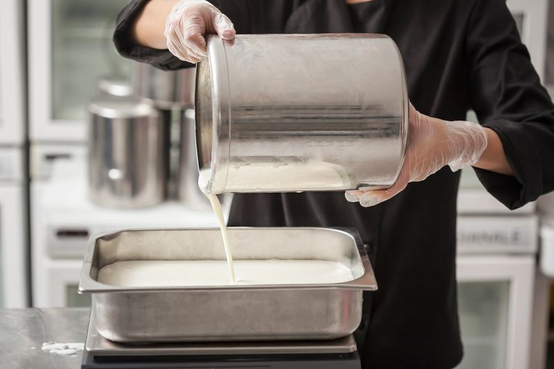 Chef with a jar filling condensed milk, making ice cream in the professional kitchen of a small manufacturing