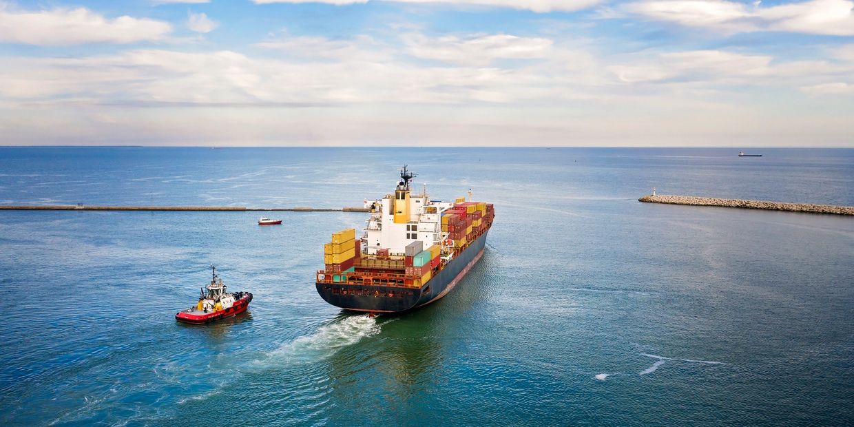 Cargo ship and tugboat on calm sea near a jetty.