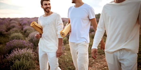 Three men walking outdoors with yoga mats in a field of flowers.
