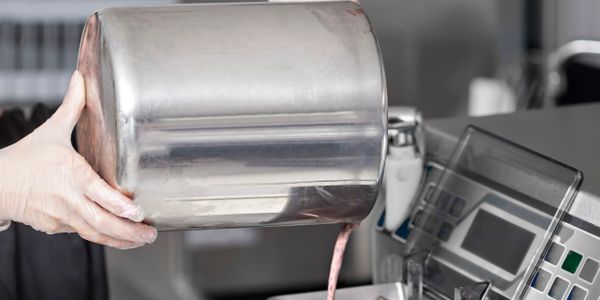 Person pouring a pink liquid from a large metal container into a machine.