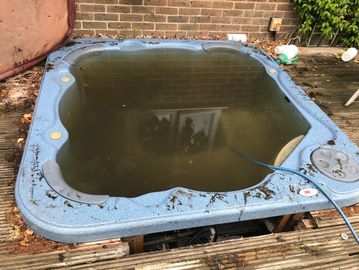 Dirty, murky water-filled hot tub with debris and hose.