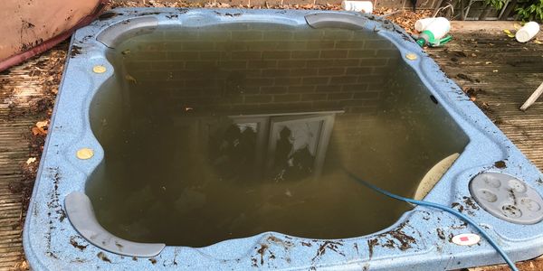 An abandoned, dirty hot tub filled with murky water on wooden decking.