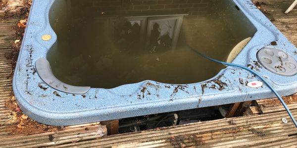 An abandoned, dirty hot tub filled with murky water on wooden decking.