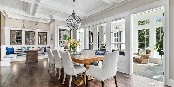 Bright dining room with wooden table and white chairs. French Doors, wood floor, coffered ceiling.