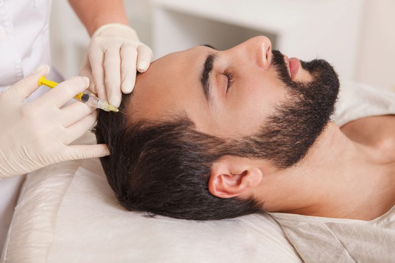 Bearded man getting anti hair loss treatment by beautician