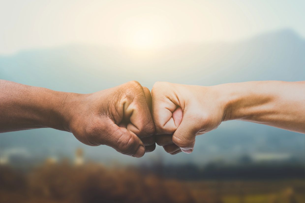 fist bump in front of sunrise over mountains