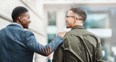 Two men smiling and walking outdoors, sharing a friendly moment.