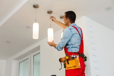 Electrician installing a hanging light fixture indoors.