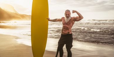 Fit elderly man posing with yellow surfboard on the beach.