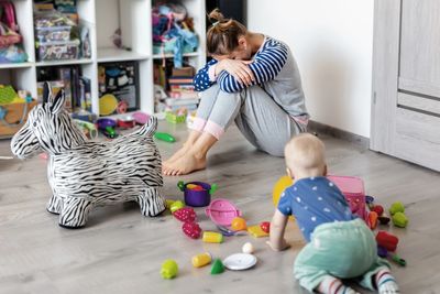 Parent épuisé assis la tête dans les mains pendant qu’un enfant crie à côté