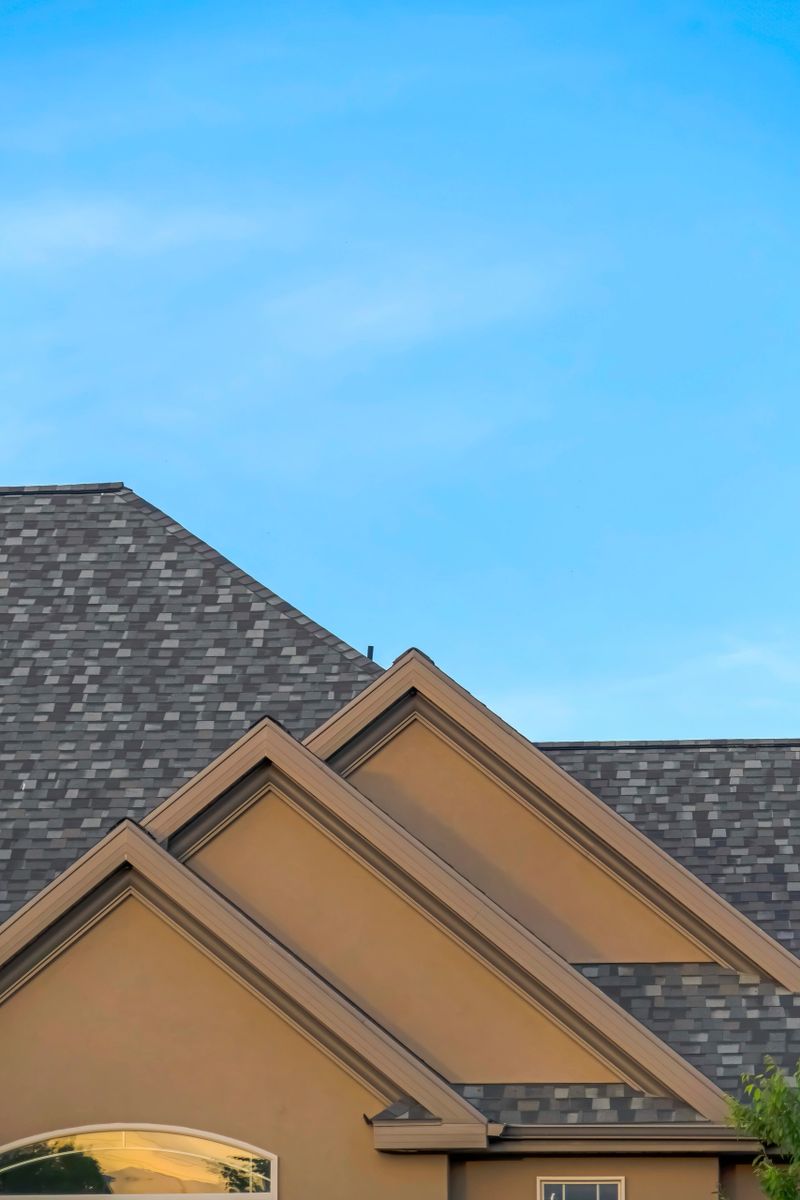 Home exterior with front gable roof and transom window against blue sky. Close up of the architectural details of the gray and pitched roof of home.