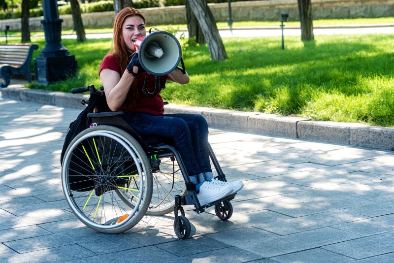 A young woman in a wheelchair with a megaphone in her hands the Concept of attracting attention and mobility for people with disabilities.