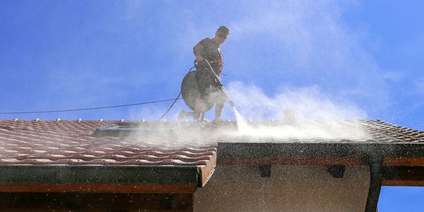 Person pressure washing a roof on a sunny day.