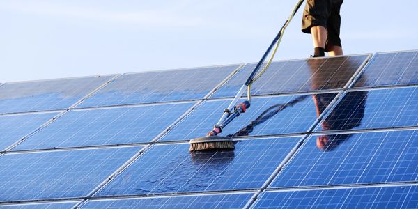 Person cleaning solar panels under clear sky.