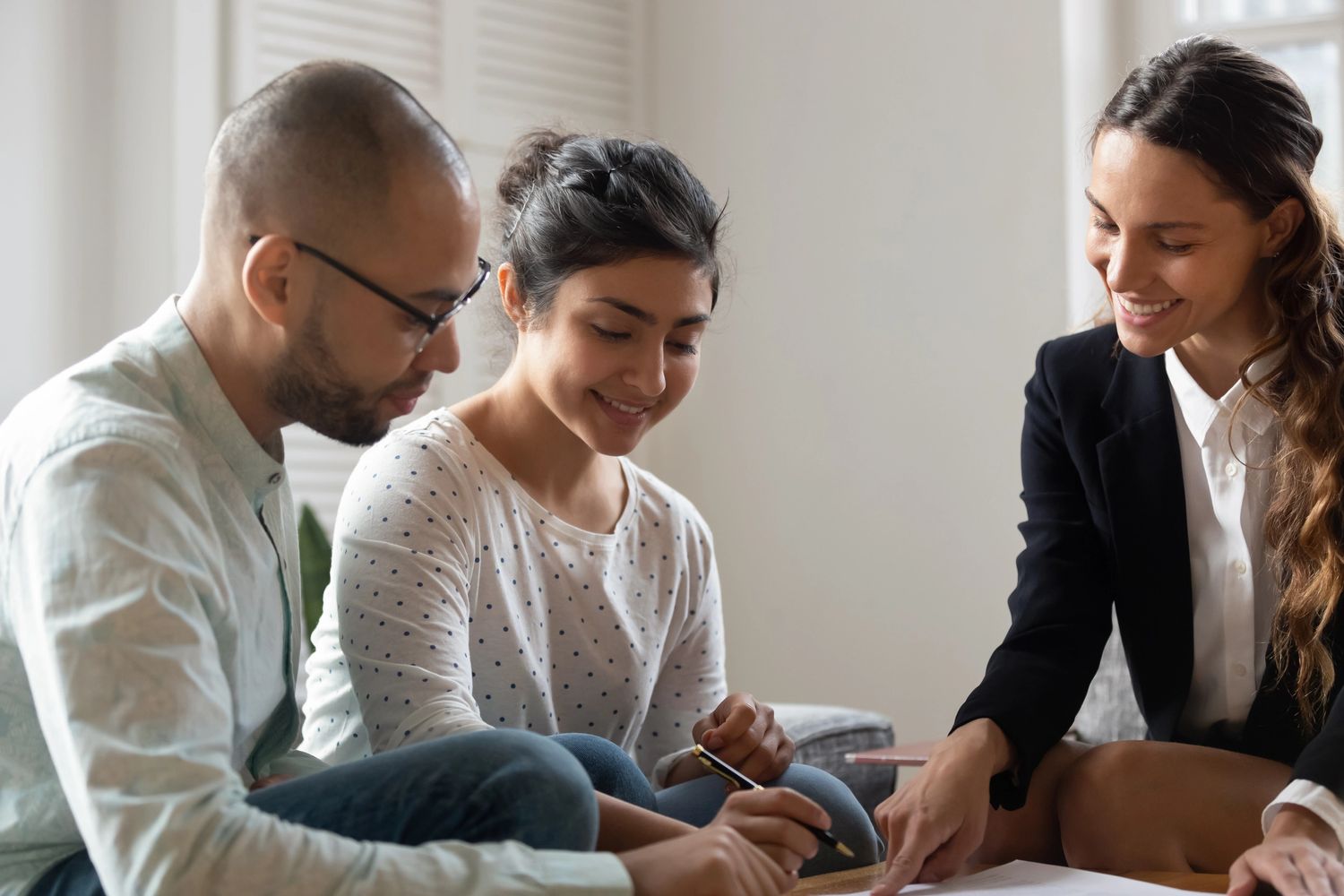 Three people collaborating on paperwork in a bright room, smiling and focused.