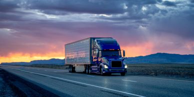 Blue semi truck on highway at sunset.
