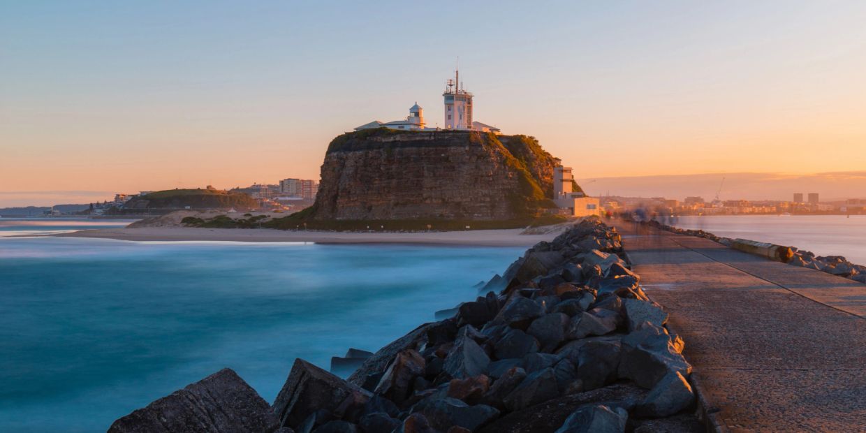 Lighthouse on rocky island at sunset.