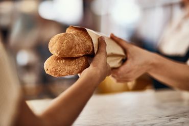 Two fresh baguettes being handed over wrapped in paper.