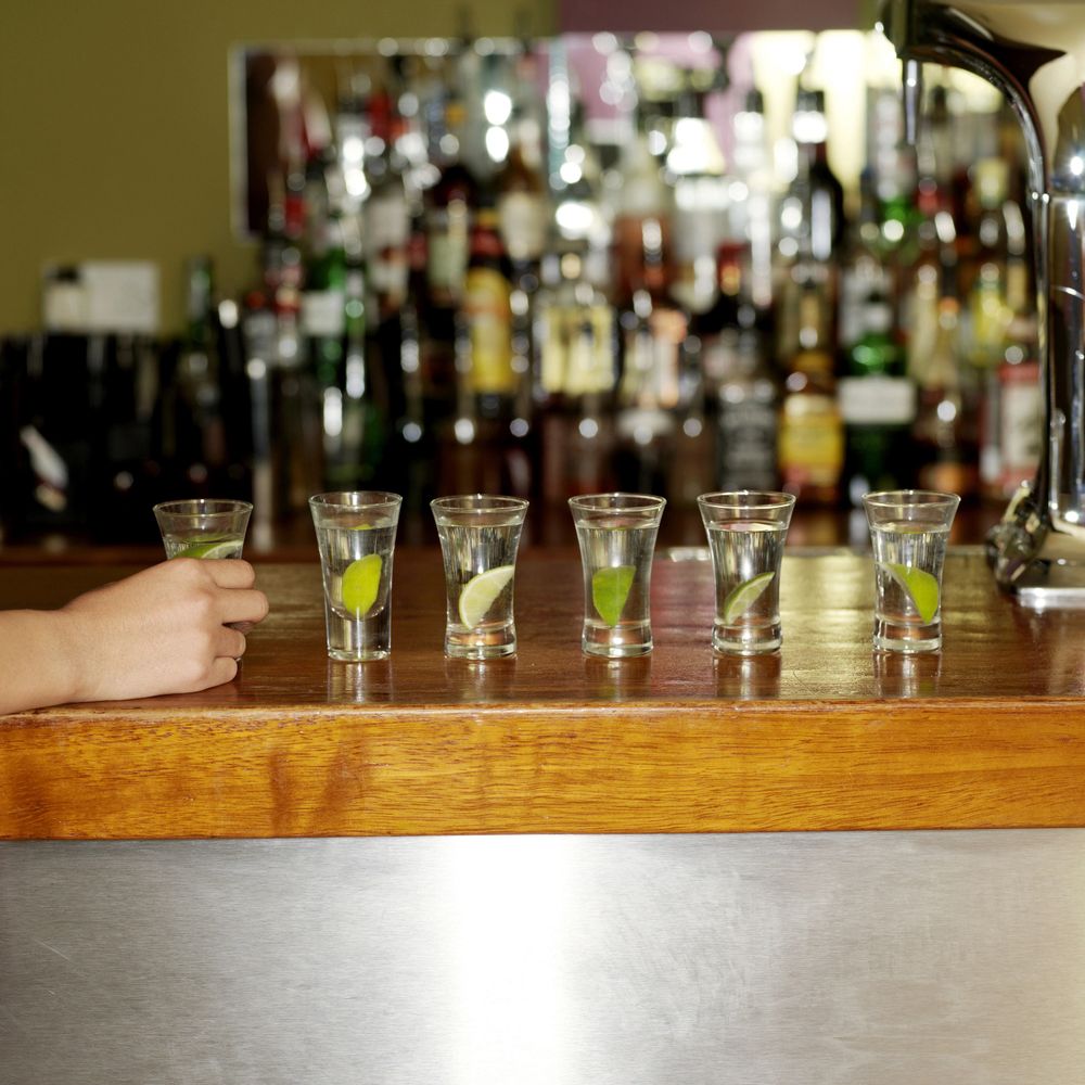 A line of six tequila shots with lime wedges on a wooden bar counter.