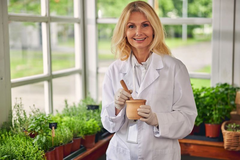 Front view of a merry mature blonde woman grinding herbal substances with a wooden pestle