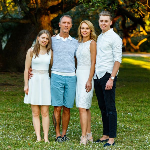 A family of four posing outdoors in coordinated white and blue outfits.