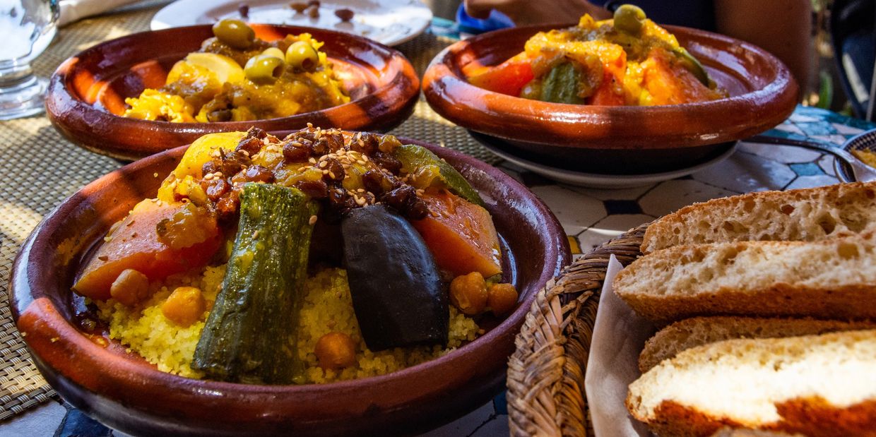 Three bowls of Moroccan couscous with vegetables and bread on the side.