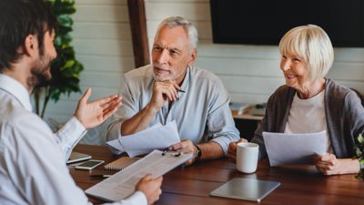A young man discussing documents with an older couple at a table.