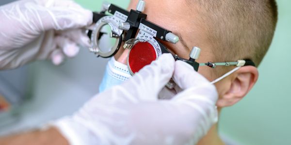 Eye test being conducted with specialized equipment on a masked patient.