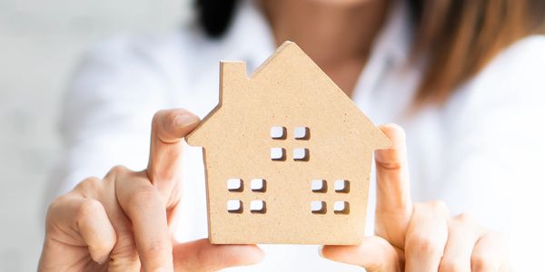Woman holding a small wooden house model and smiling.