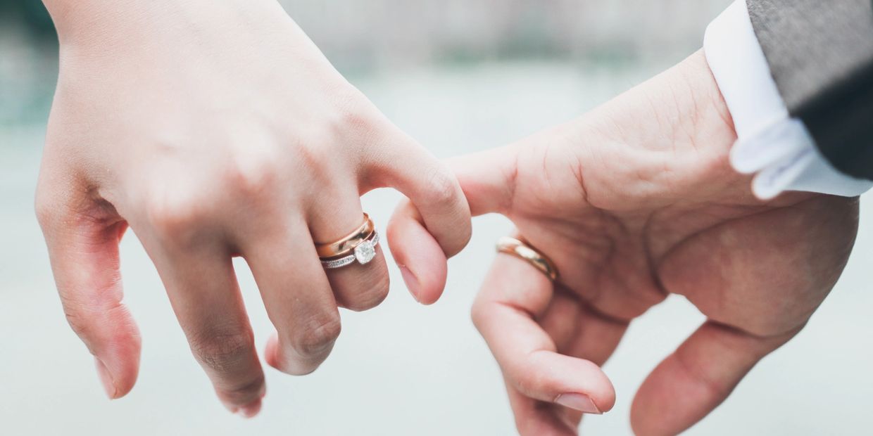 Couple holding pinky fingers, both wearing wedding rings.