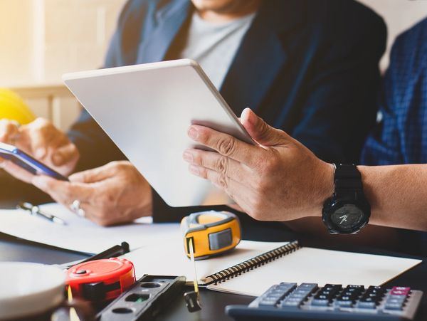 Two people reviewing construction plans using a tablet and smartphone.