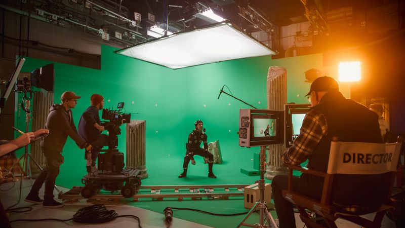 In the Big Film Studio Professional Crew Shooting Blockbuster Movie. Director Commands Camera Operator to Start shooting Green Screen CGI Scene with Actor Wearing Motion Tracking Suit and Head Rig