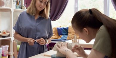 A woman watches another paint pottery in a cozy studio.
