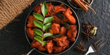 Spicy fried chicken pieces garnished with curry leaves and accompanied by whole spices.