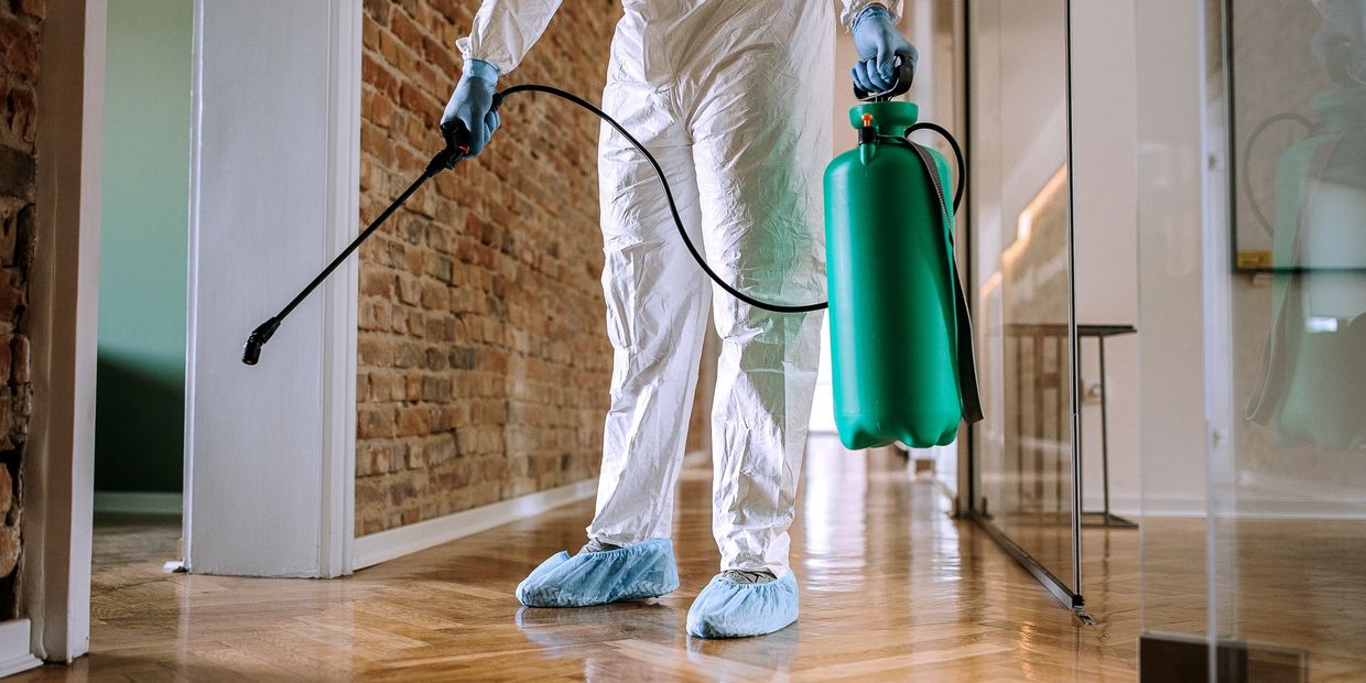Person in protective gear spraying disinfectant indoors.