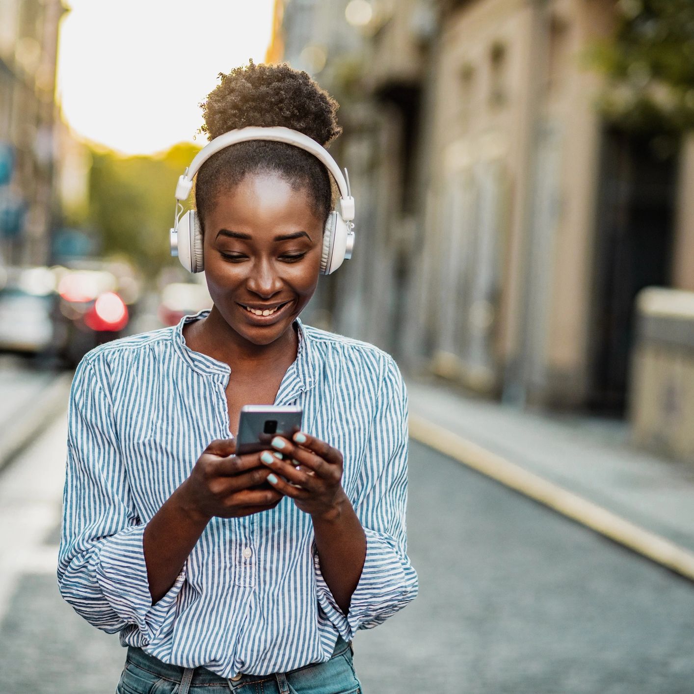 Woman smiling while using phone and wearing headphones.