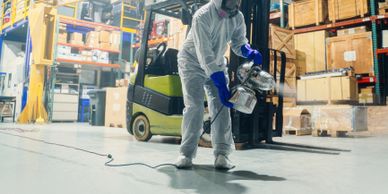 Worker in protective gear disinfecting a warehouse with a fogging machine.