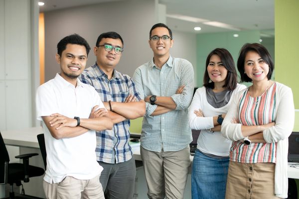 Five smiling coworkers stand with crossed arms in a modern office.