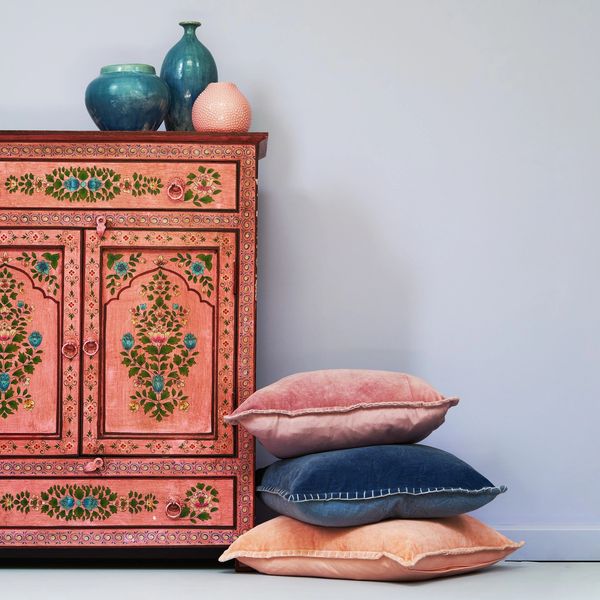 Decorative pink cabinet with floral designs next to stacked velvet cushions.