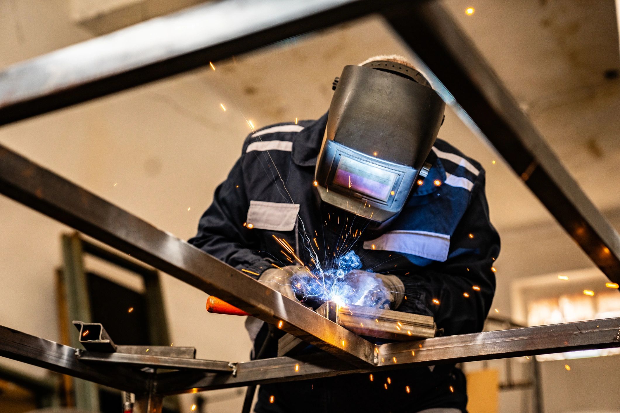 Person welding metal with protective gear and sparks flying.