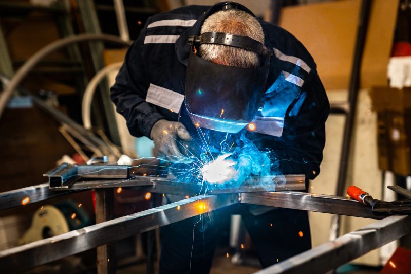 Senior man welding metal construction at work place.  He is dressed in full protective suit.
