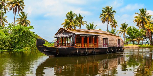 Traditional houseboat floating on calm water with palm trees in the background.